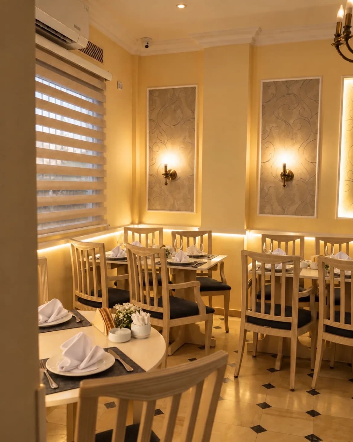 La salle de jour, stores baissés, tables dressées sous les appliques.